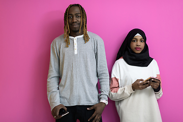 Image showing young african american couple laughing using smartphones apps isolated on pink studio background