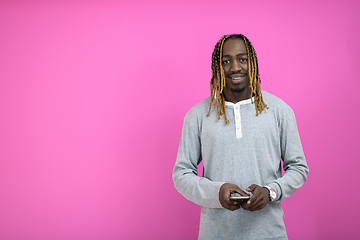 Image showing afro guy uses a phone while posing in front of a pink background.