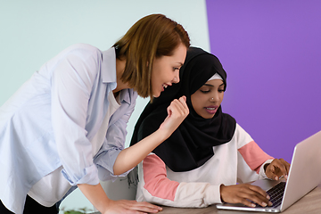 Image showing afro muslim woman wearing a hijab sits smiling in her home office and using laptop for online meeting