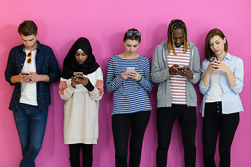 Image showing diverse teenagers use mobile devices while posing for a studio photo in front of a pink background