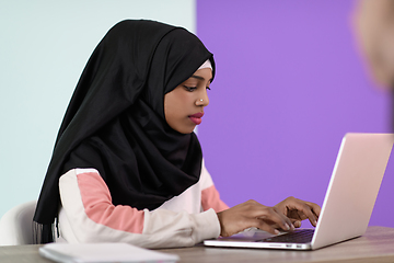 Image showing afro girl wearing a hijab thoughtfully sits in her home office and uses a laptop