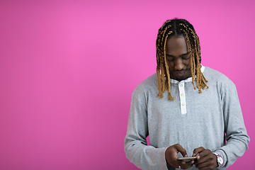 Image showing afro guy uses a phone while posing in front of a pink background.