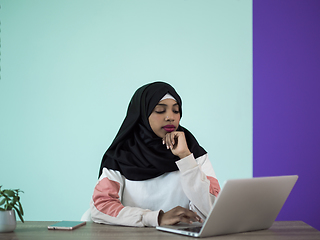 Image showing afro girl wearing a hijab thoughtfully sits in her home office and uses a laptop