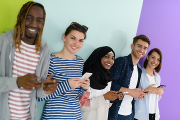 Image showing diverse teenagers use mobile devices while posing for a studio photo in front of a pink background