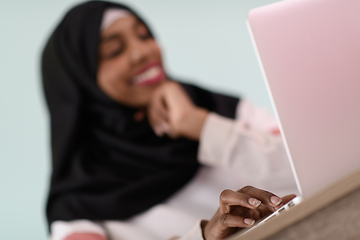 Image showing afro muslim woman wearing a hijab sits smiling in her home office and uses a laptop