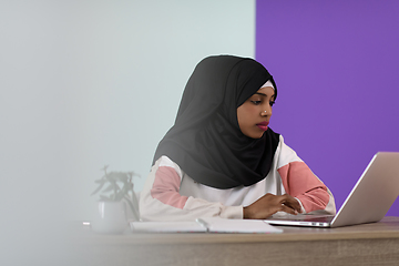 Image showing afro girl wearing a hijab thoughtfully sits in her home office and uses a laptop