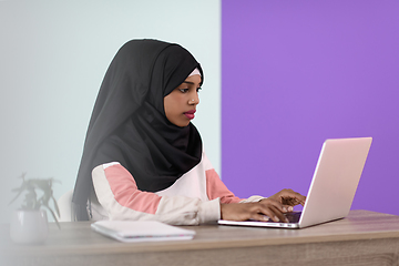 Image showing afro girl wearing a hijab thoughtfully sits in her home office and uses a laptop