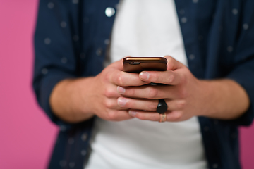 Image showing a young man using a smartphone on a pink background.