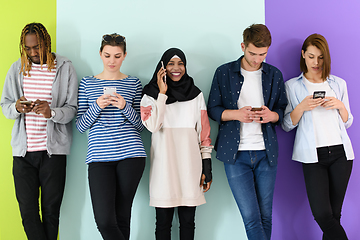 Image showing diverse teenagers use mobile devices while posing for a studio photo in front of a pink background