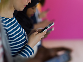 Image showing diverse teenagers use mobile devices while posing for a studio photo in front of a pink background