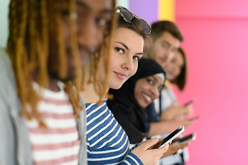 Image showing diverse teenagers use mobile devices while posing for a studio photo in front of a pink background