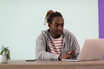 Image showing an afro young man sits in his home office during a pandemic and uses laptop