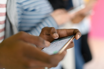 Image showing diverse teenagers use mobile devices while posing for a studio photo in front of a pink background