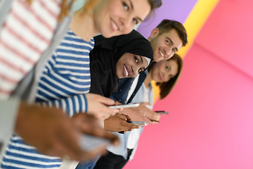 Image showing diverse teenagers use mobile devices while posing for a studio photo in front of a pink background