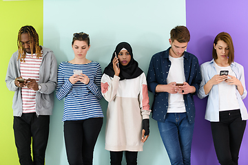 Image showing diverse teenagers use mobile devices while posing for a studio photo in front of a pink background