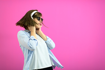 Image showing brunette lady in black glasses dancing and listening music isolate on pink background