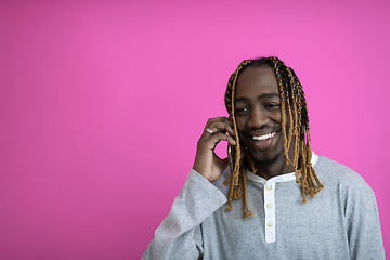 Image showing afro guy uses a phone while posing in front of a pink background.