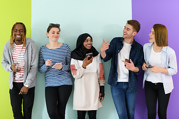 Image showing diverse teenagers use mobile devices while posing for a studio photo in front of a pink background