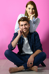 Image showing couple sitting on the floor while posing in front of a pink background