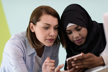 Image showing afro girl with a hijab and a European woman use a cell phone and laptop in their home office