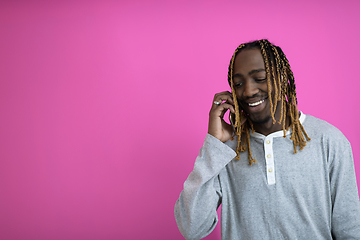 Image showing afro guy uses a phone while posing in front of a pink background.