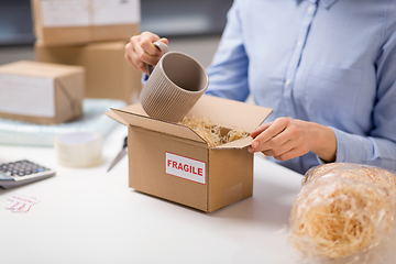 Image showing woman packing mug to parcel box at post office