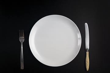 Image showing Fork, knife and white plate on black background in flat lay