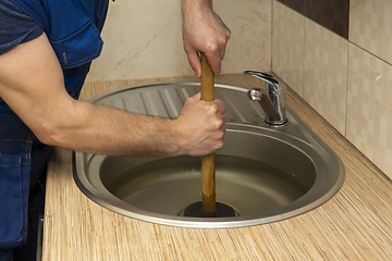 Image showing A plumber clear a blockage in a kitchen sink with a plunger