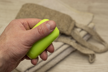 Image showing A piece of soap in hand on background of a terry towel and washcloth