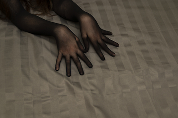 Image showing Graceful female hands in black seductive nylon gloves on bedsheet