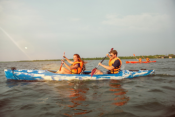 Image showing Happy friends kayaking on river with sunset on the background