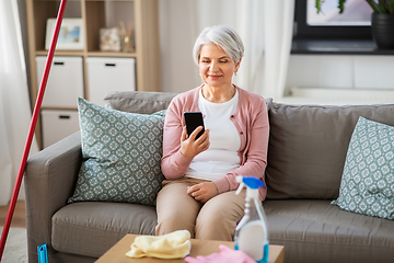 Image showing senior woman using smartphone after cleaning home