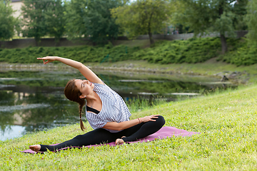 Image showing Young beautiful woman doing yoga exercise in green park. Healthy lifestyle and fitness concept.