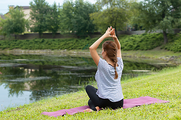 Image showing Young beautiful woman doing yoga exercise in green park. Healthy lifestyle and fitness concept.