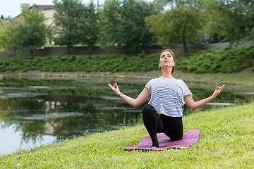 Image showing Young beautiful woman doing yoga exercise in green park. Healthy lifestyle and fitness concept.