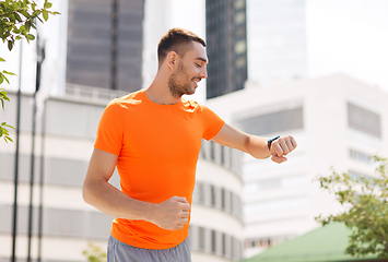 Image showing smiling young man with smart watch running at city