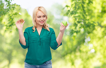 Image showing smiling woman choosing between apple and cookie