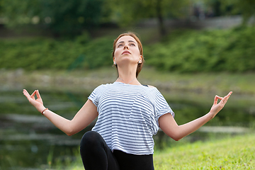 Image showing Young beautiful woman doing yoga exercise in green park. Healthy lifestyle and fitness concept.