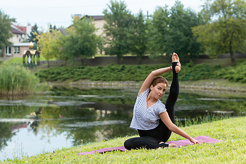 Image showing Young beautiful woman doing yoga exercise in green park. Healthy lifestyle and fitness concept.