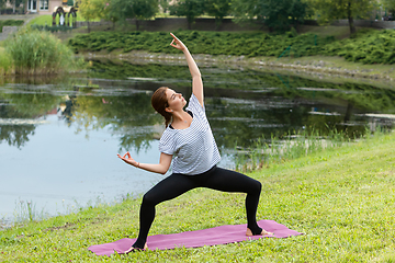 Image showing Young beautiful woman doing yoga exercise in green park. Healthy lifestyle and fitness concept.