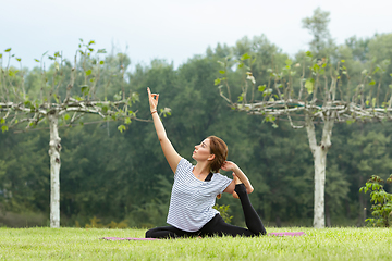 Image showing Young beautiful woman doing yoga exercise in green park. Healthy lifestyle and fitness concept.