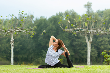 Image showing Young beautiful woman doing yoga exercise in green park. Healthy lifestyle and fitness concept.