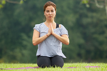 Image showing Young beautiful woman doing yoga exercise in green park. Healthy lifestyle and fitness concept.