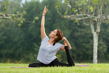 Image showing Young beautiful woman doing yoga exercise in green park. Healthy lifestyle and fitness concept.