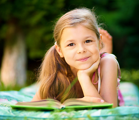 Image showing Little girl is reading a book outdoors