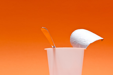 Image showing empty clean yogurt cup with spoon on an orange background