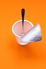 Image showing empty clean yogurt cup with spoon on an orange background