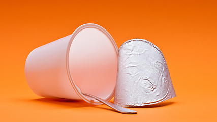 Image showing empty clean yogurt cup with spoon on an orange background