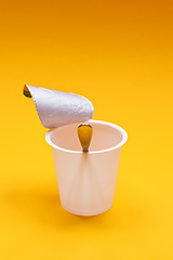 Image showing empty clean yogurt cup with spoon on an orange background