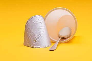 Image showing empty clean yogurt cup with spoon on an orange background